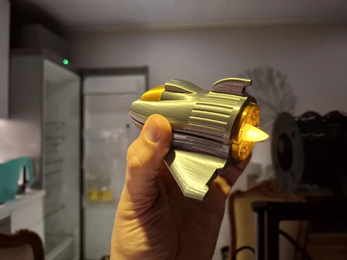 A hand holds a small, gold-colored, rocket-shaped object with a glowing orange tip, resembling a toy or novelty item. The…