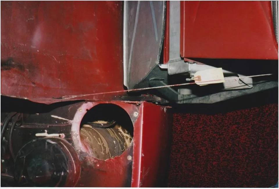 A close-up photo shows the interior of a red vehicle, possibly a train or bus, with a torn panel revealing a messy, dark…