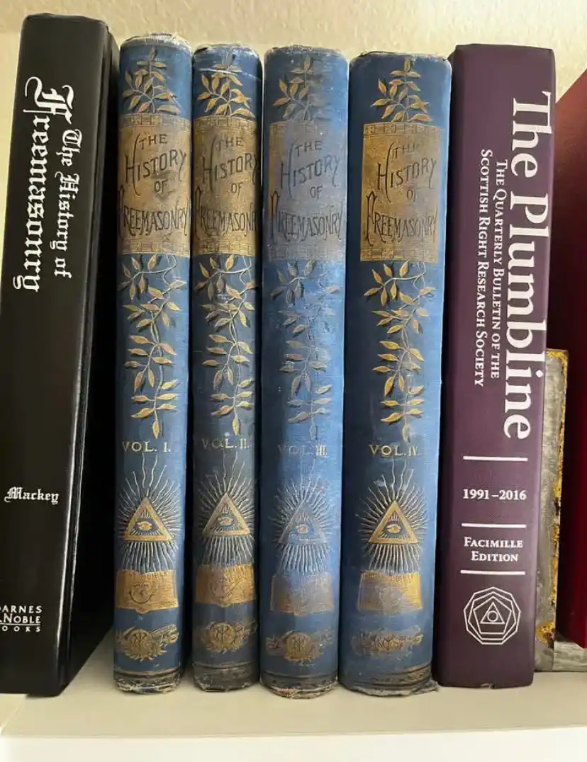 A bookshelf displays five volumes of 'The History of Freemasonry' with ornate blue spines featuring gold leaf patterns and…
