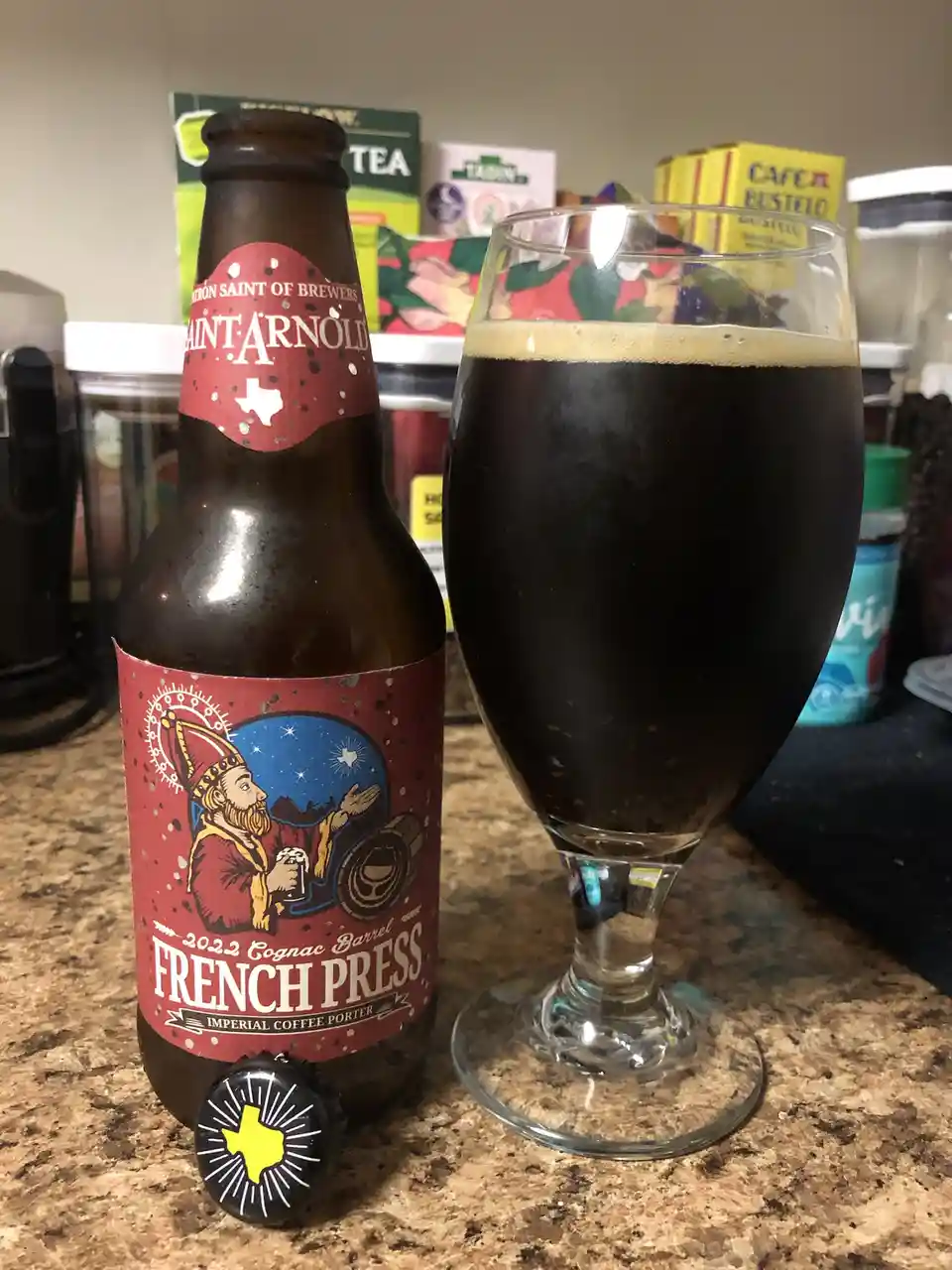 A brown glass bottle of Saint Arnold 2022 Cognac Barrel French Press Imperial Coffee Porter sits next to a glass filled with…