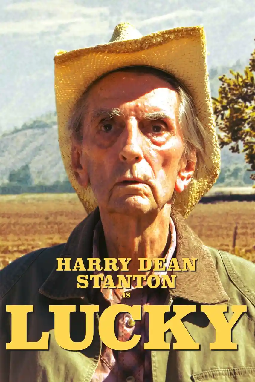 An older man with weathered skin and a straw cowboy hat stares intensely at the camera against a backdrop of dry fields and…