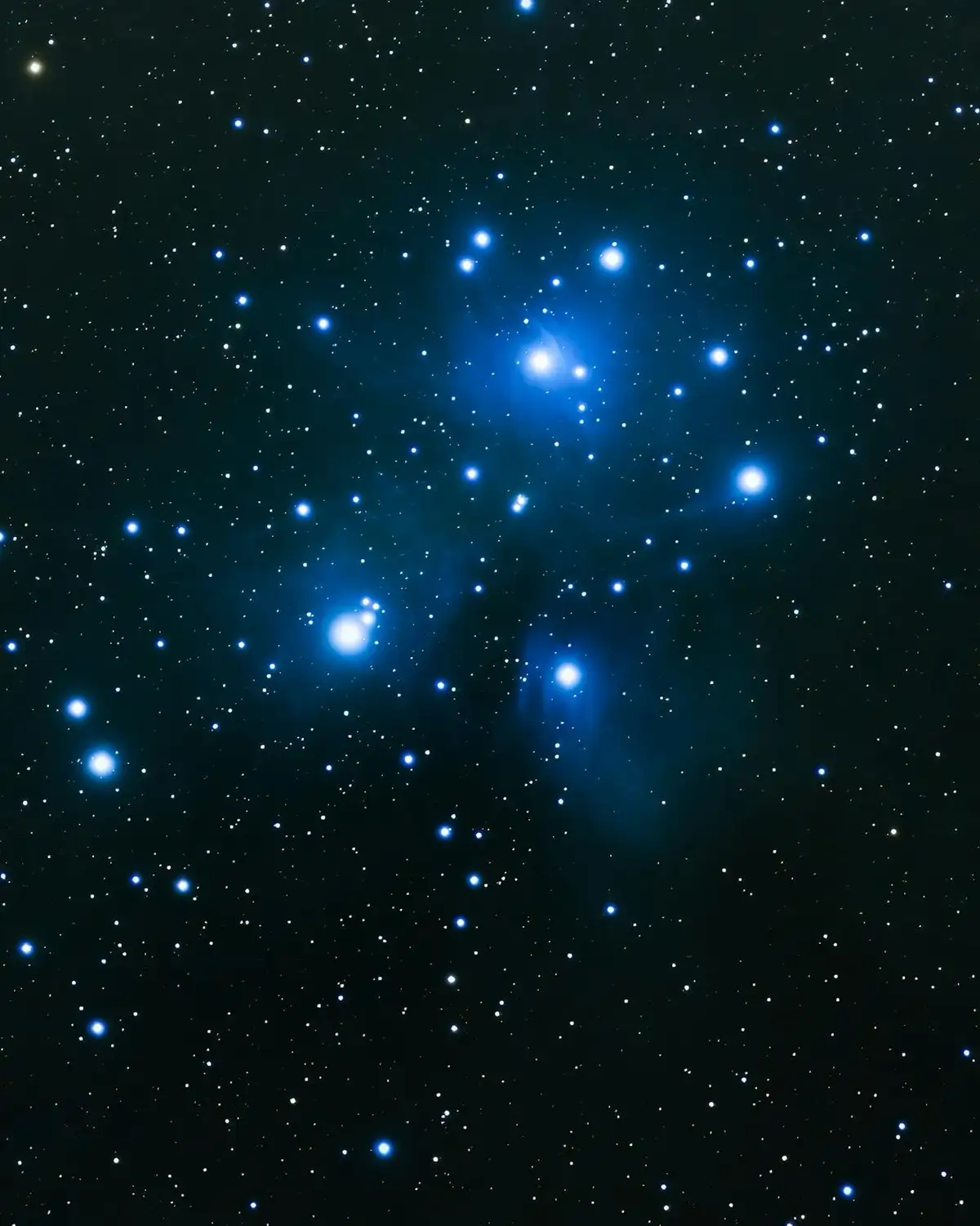 A deep space photograph shows a dense cluster of bright blue stars against a dark background, with some stars appearing as…