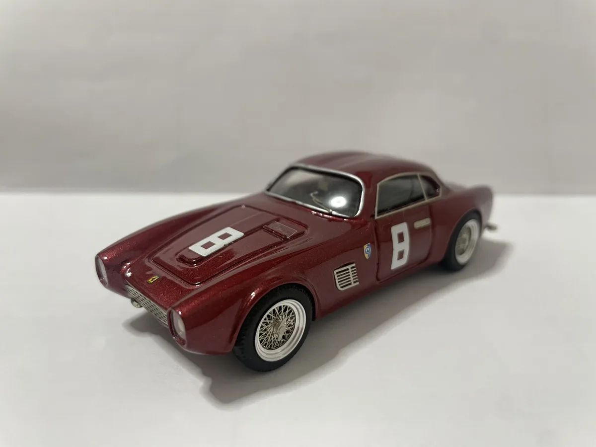 A maroon die-cast model of a vintage Ferrari race car, featuring the number 8 prominently displayed in white on both the…
