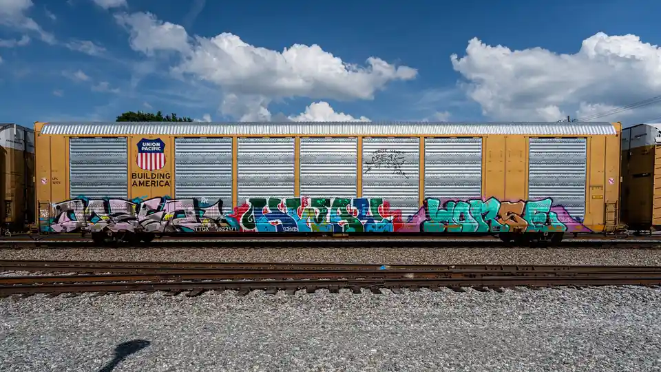 A yellow Union Pacific freight train car with 'Building America' branding sits on tracks under a blue sky with clouds. The…