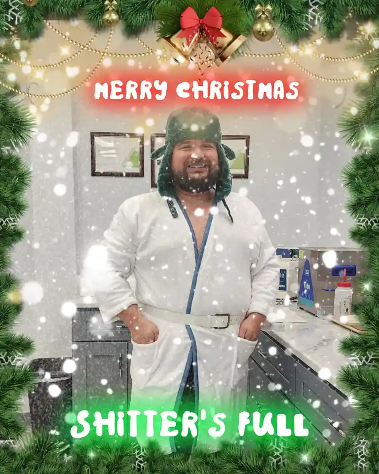 A man in a white bathrobe and green winter hat stands in a kitchen with snow falling around him. The image is framed with…