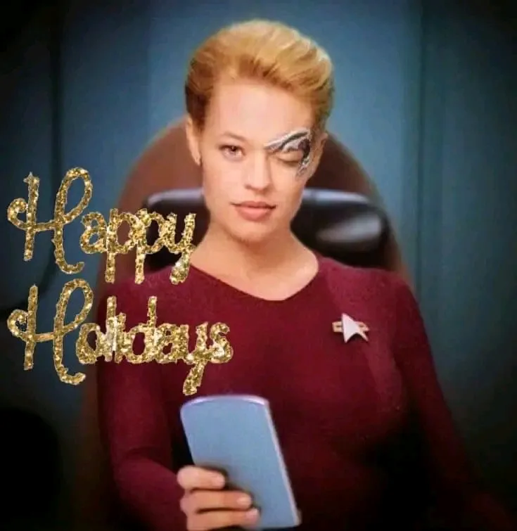 A woman in a Star Trek uniform with a glittery eye patch looks down at a phone while the text 'Happy Holidays' appears in…