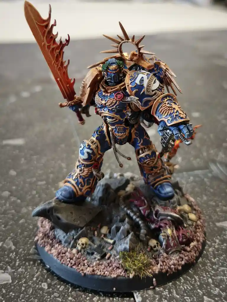 A highly detailed, hand-painted miniature of a blue and gold armored warrior, likely from Warhammer 40,000, stands on a…