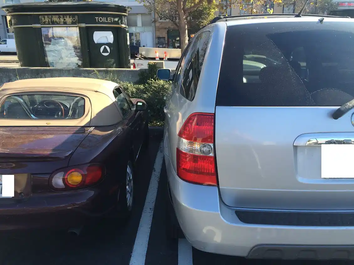 Two cars are parked side-by-side in a parking lot, with a small gap between them. The car on the left is a maroon…