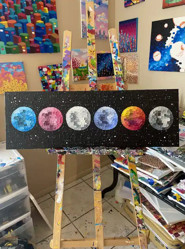 A painting on an easel depicts six planets in a row against a black, textured starry background, each rendered with a thick…