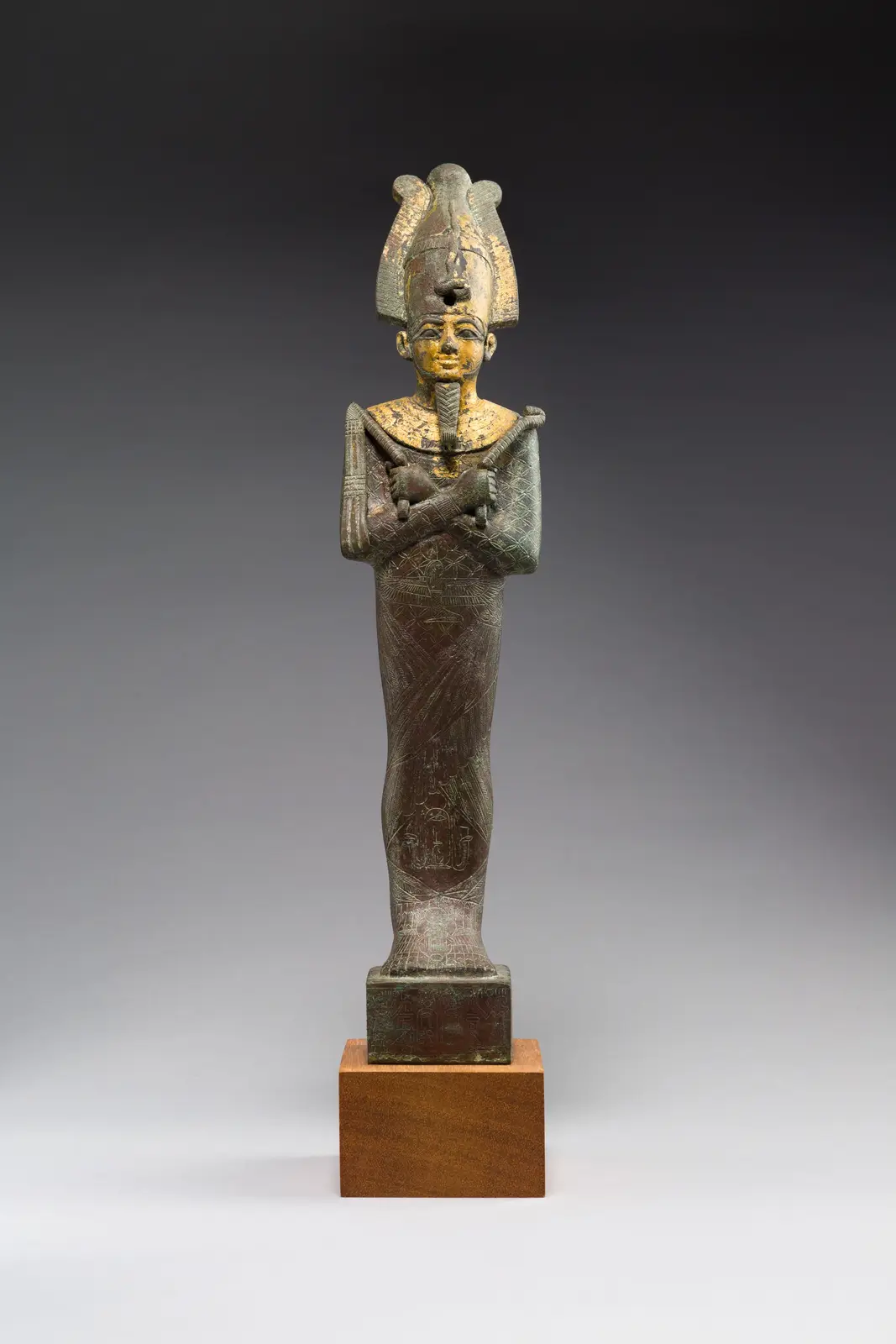 A full-length ancient Egyptian statue of a pharaoh, likely made of bronze with gold leaf remnants, stands on a wooden…