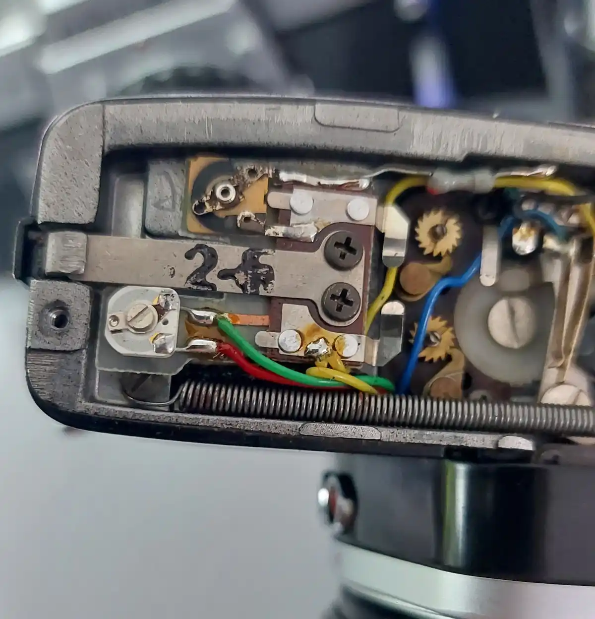 A close-up shot of the internal mechanism of an old, worn electronic device, revealing corroded metal parts, tangled wires…