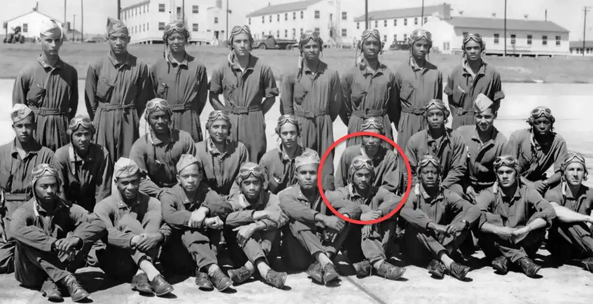 A black-and-white historical photo shows a group of African American military pilots in uniform posing for a group photo…