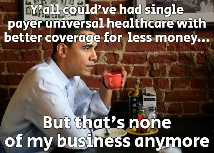 A man in a light blue shirt sits at a table with a red mug, looking off to the side with a thoughtful or resigned…