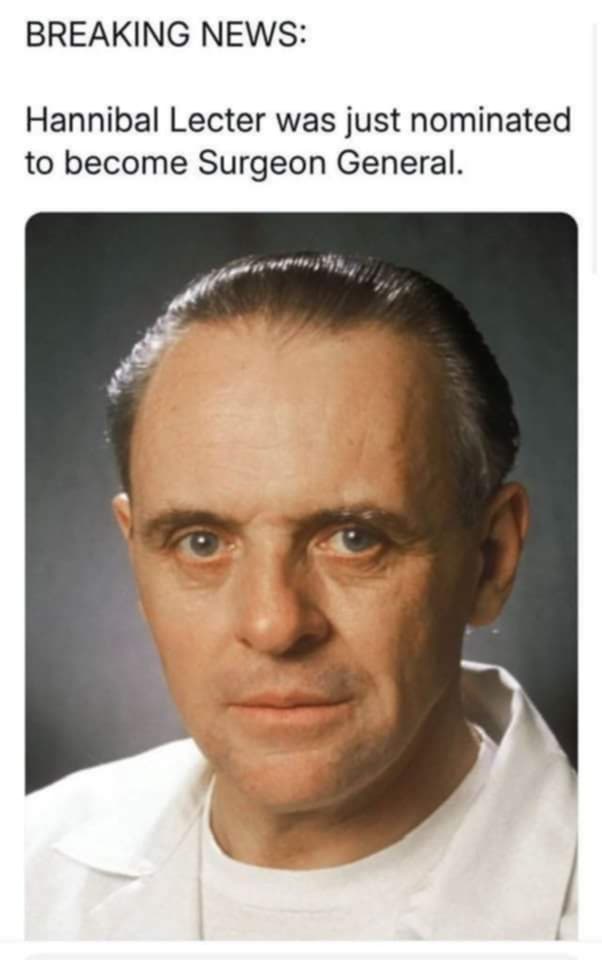 A still image of actor Anthony Hopkins as Hannibal Lecter, wearing a white lab coat over a white t-shirt, with a serious…