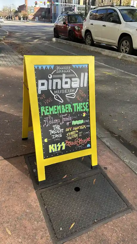 A yellow-framed chalkboard sign for a 'Classic Arcade Pinball Museum' lists iconic pinball games like 'The Addams Family'…