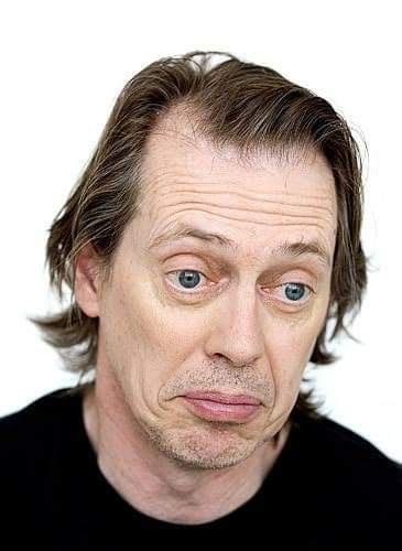 A close-up portrait of a man with wide, startled eyes and a slightly downturned mouth, wearing a black shirt against a plain…
