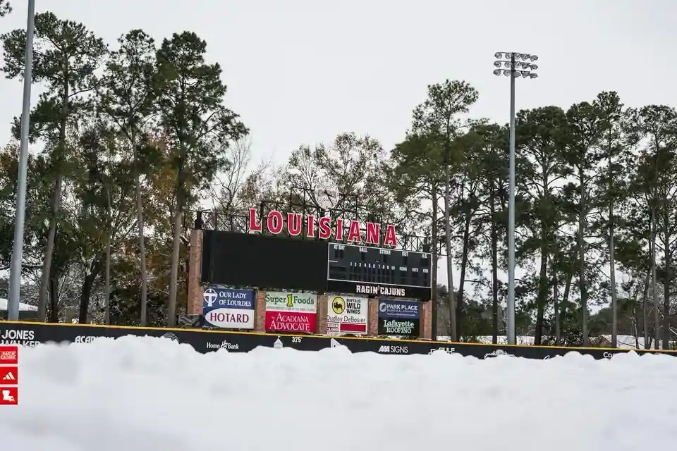 A baseball stadium scoreboard with 'LOUISIANA' and 'RAGIN' CAJUNS' visible is completely buried under a thick layer of snow…