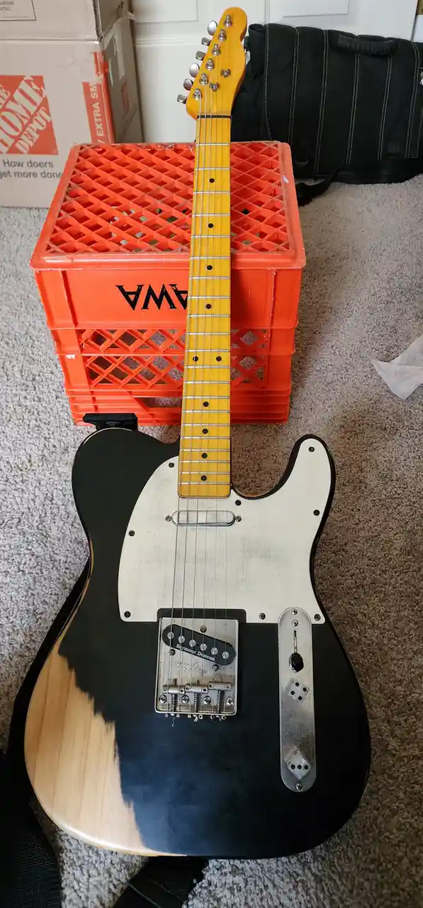 A black and natural wood-finish electric guitar with a white pickguard and a Seymour Duncan pickup is propped upright…