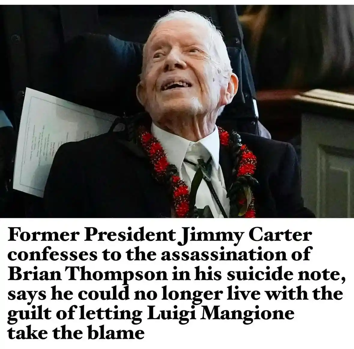An elderly man with white hair, wearing a dark suit, white shirt, and a red lei, is seated in a wheelchair and smiling…