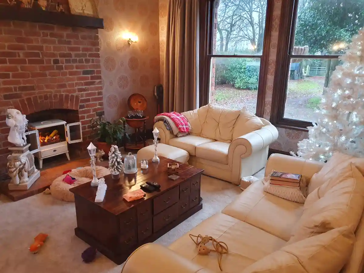 A cozy, well-decorated living room with beige leather sofas, a wooden coffee table, a brick fireplace with a lit stove, and…