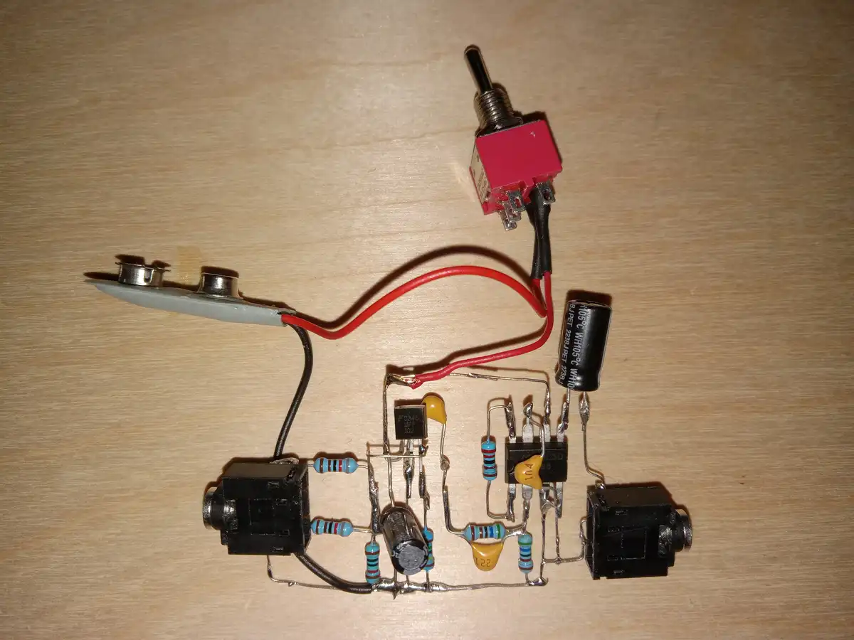 A hand-built electronic circuit on a wooden surface features a red toggle switch, resistors, capacitors, transistors, and…