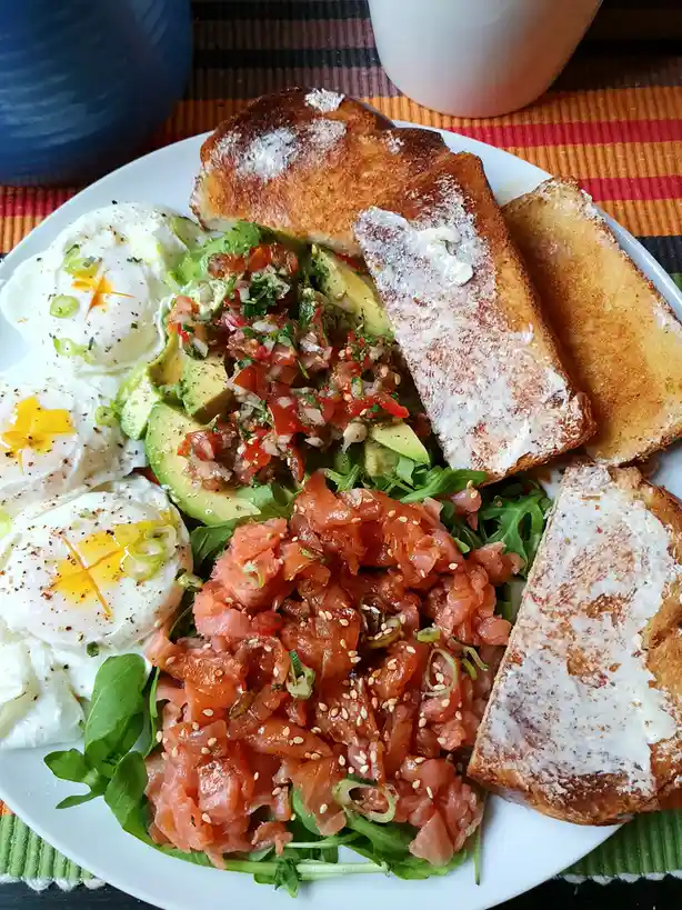 A white plate holds a colorful, healthy-looking breakfast featuring three poached eggs with runny yolks, avocado slices…