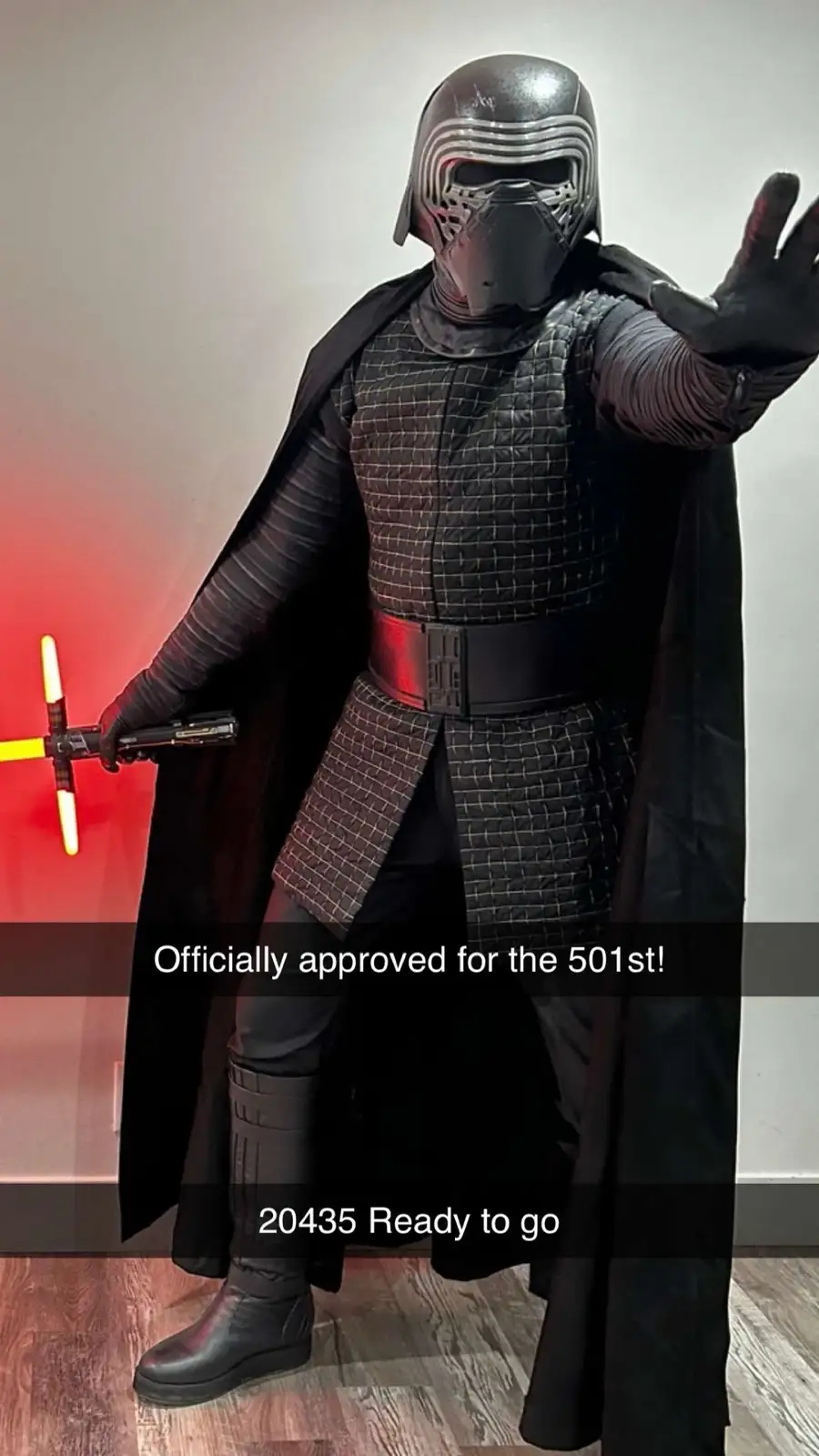 A person in a full Kylo Ren costume from Star Wars, holding a yellow lightsaber and posing with one hand outstretched. The…