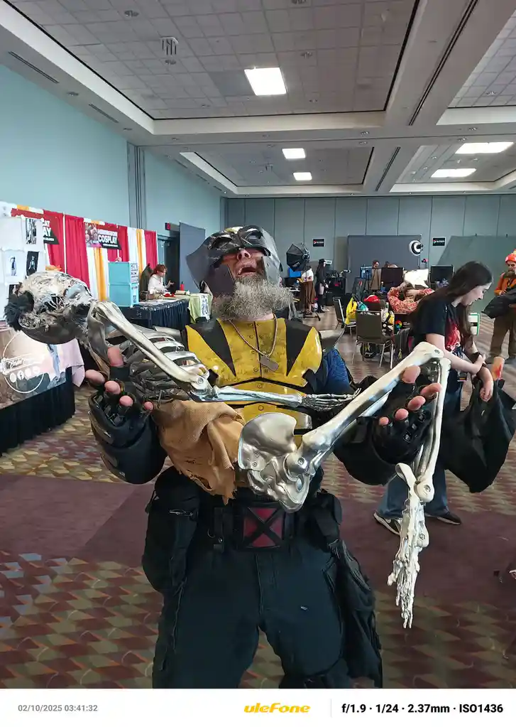 A man in a detailed costume resembling a skeletal warrior with metallic bones for arms and a skull headpiece, holding up his…
