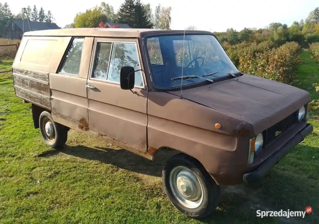 A rusty, brown, boxy van with a wooden rear section is parked on grass, showing visible wear and tear. The overlaid text…