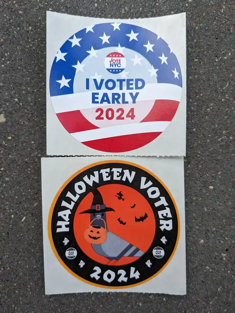Two circular stickers lie on asphalt. The top one features an American flag design with 'I VOTED EARLY 2024' and a 'VOTE…