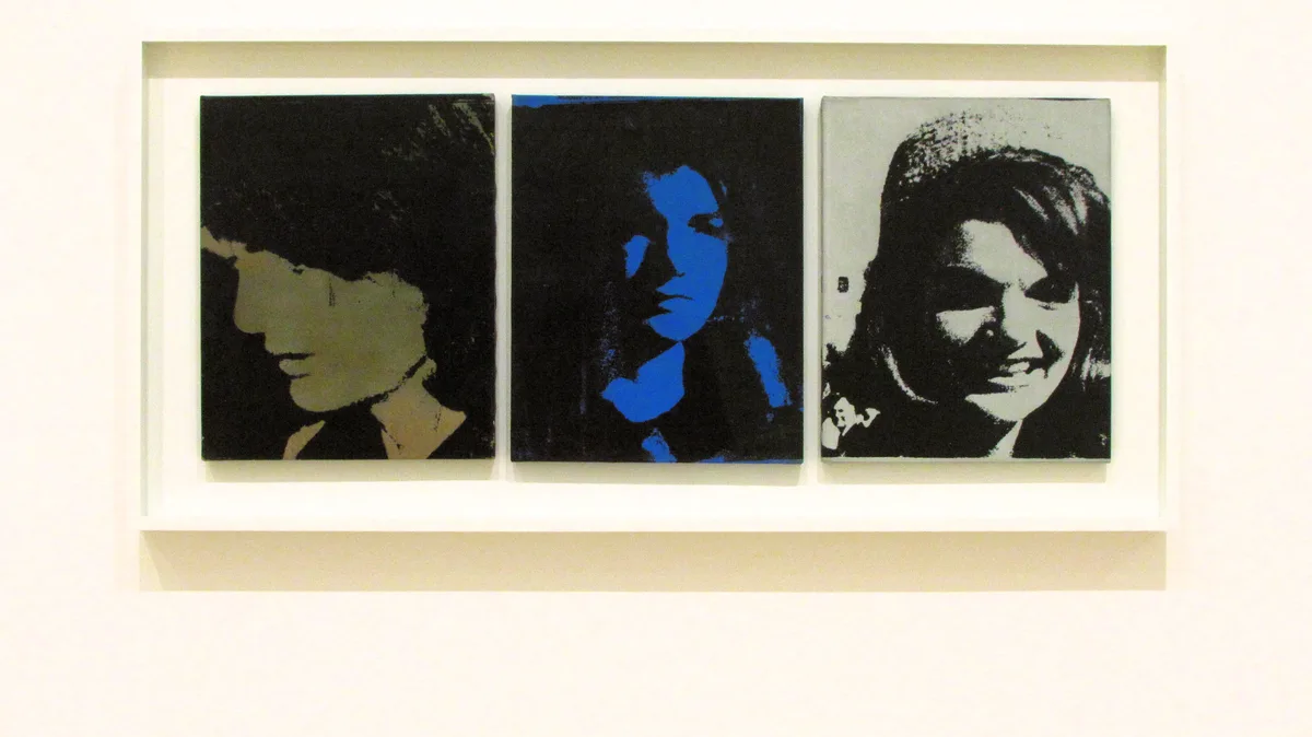 Three framed pop art portraits of a woman are displayed side-by-side on a white wall. The left portrait is a beige and black…
