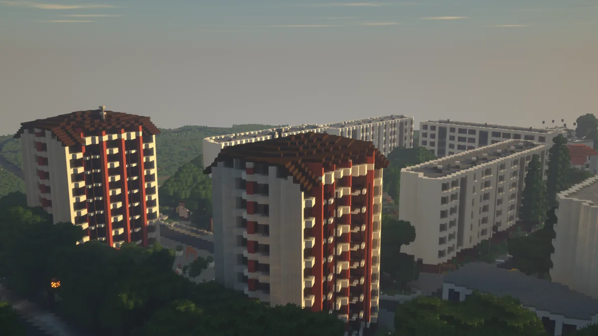 A screenshot from the game Minecraft showing a cityscape of blocky apartment buildings with red and beige facades…