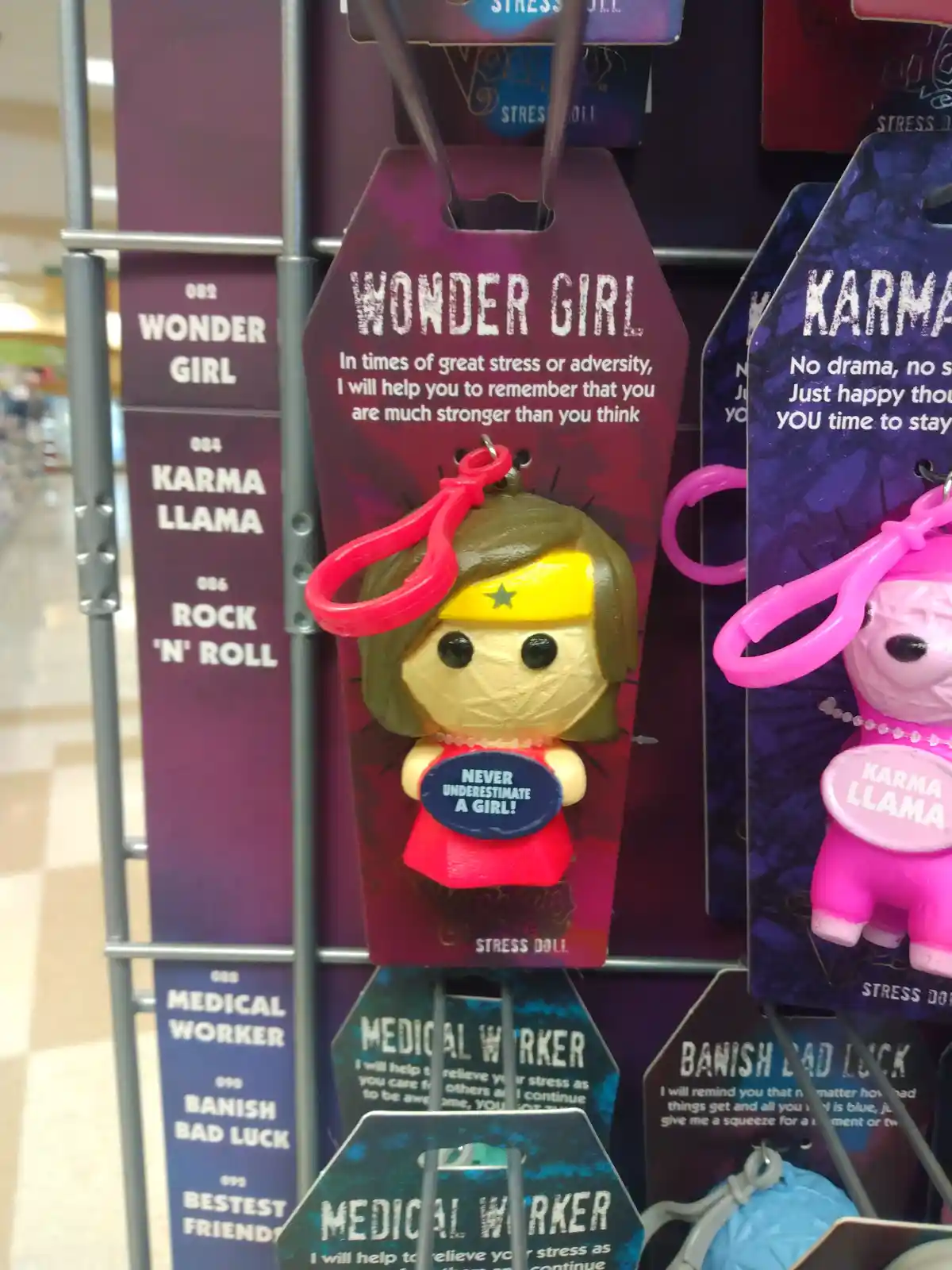A close-up of a store shelf displaying stress-relief dolls, with a Wonder Girl doll in the center holding a sign that reads…