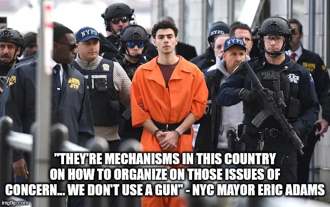 A man in an orange prison jumpsuit stands center-frame surrounded by multiple NYPD officers in tactical gear, some holding…
