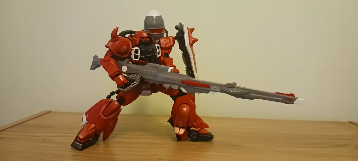A red and grey robot toy stands on a wooden surface holding a large rifle and a shield, with overlaid text reading 'i'm not…