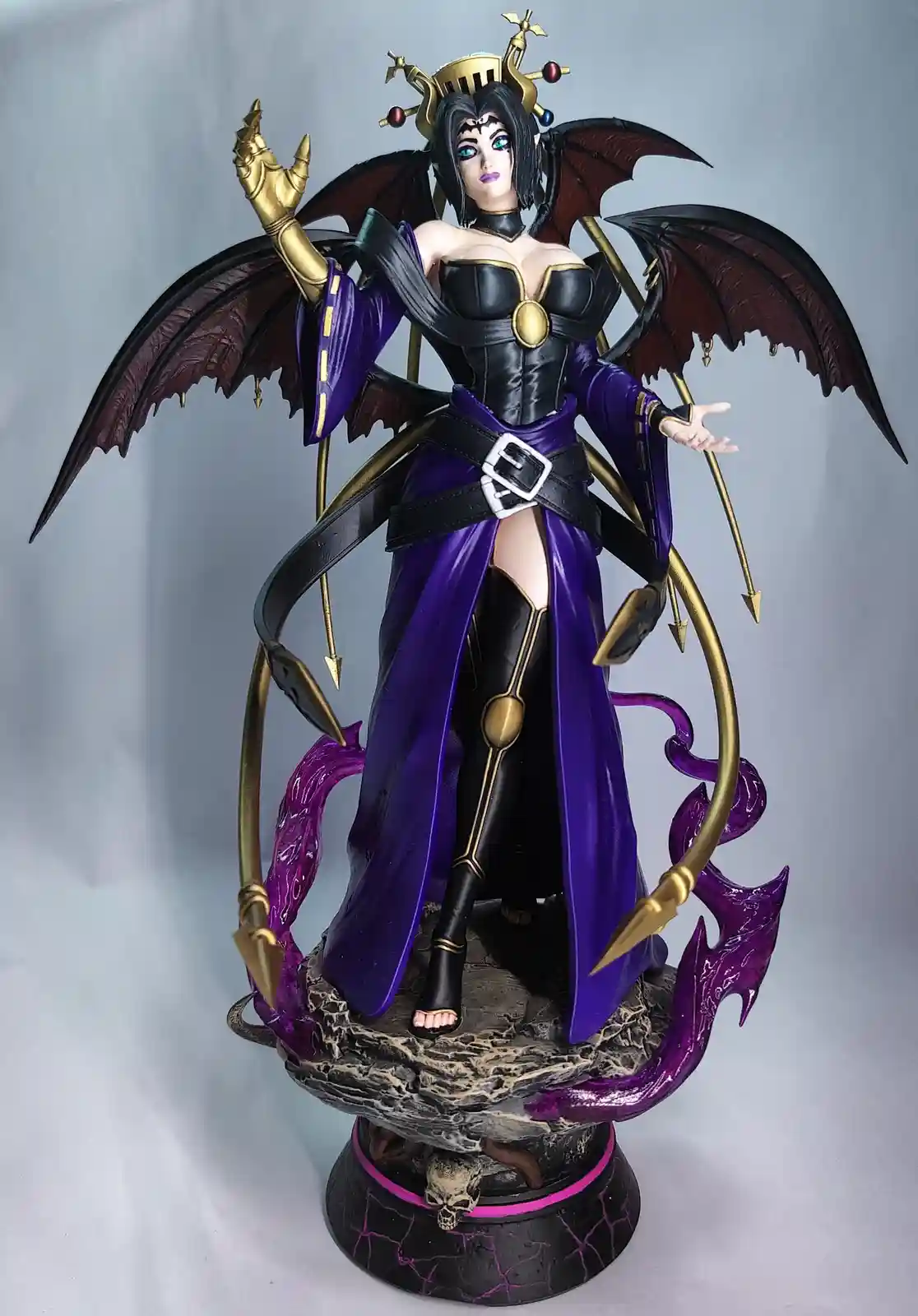 A detailed figurine of a dark fantasy female character with black hair, bat-like wings, and a purple and black outfit…