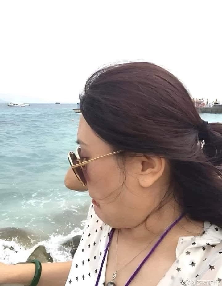 一张海边自拍，一位女士侧脸对着镜头，戴着金色边框太阳镜，背景是海面和远处的船只。她的鼻子被明显地拉长和夸张化，形成一个滑稽的突起。图片右下角有微博水印。图片上叠加的文字是“我老公说他要给我买个新鼻子”。