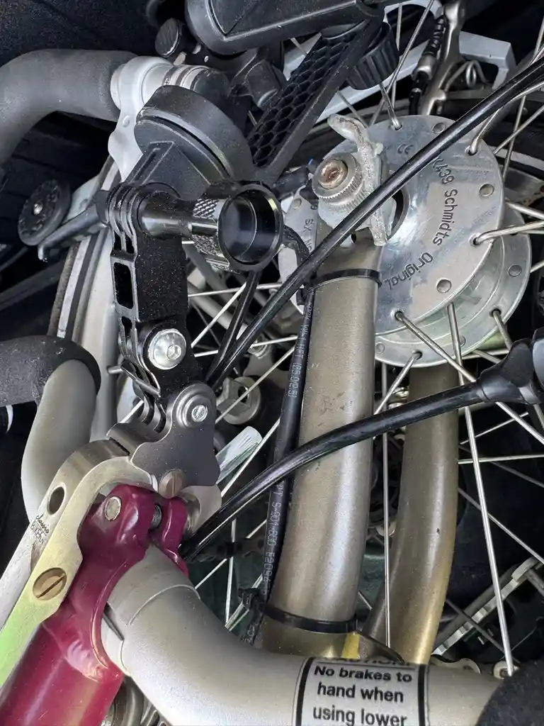 A close-up photo of a bicycle's front wheel and fork, showing a complex tangle of wires, a brake lever, and a red-handled…