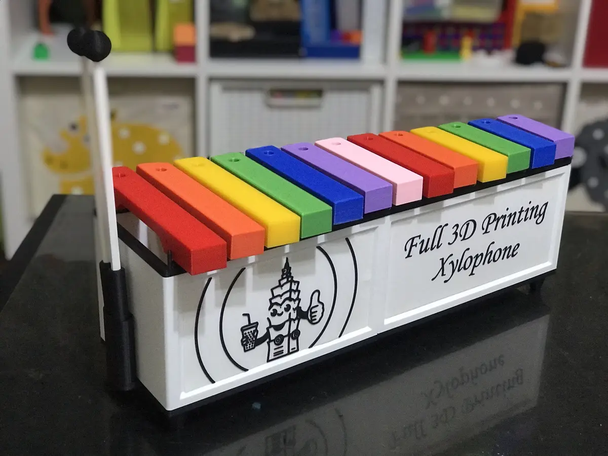 A colorful xylophone with rainbow keys sits on a black surface, its white body labeled 'Full 3D Printing Xylophone' and…