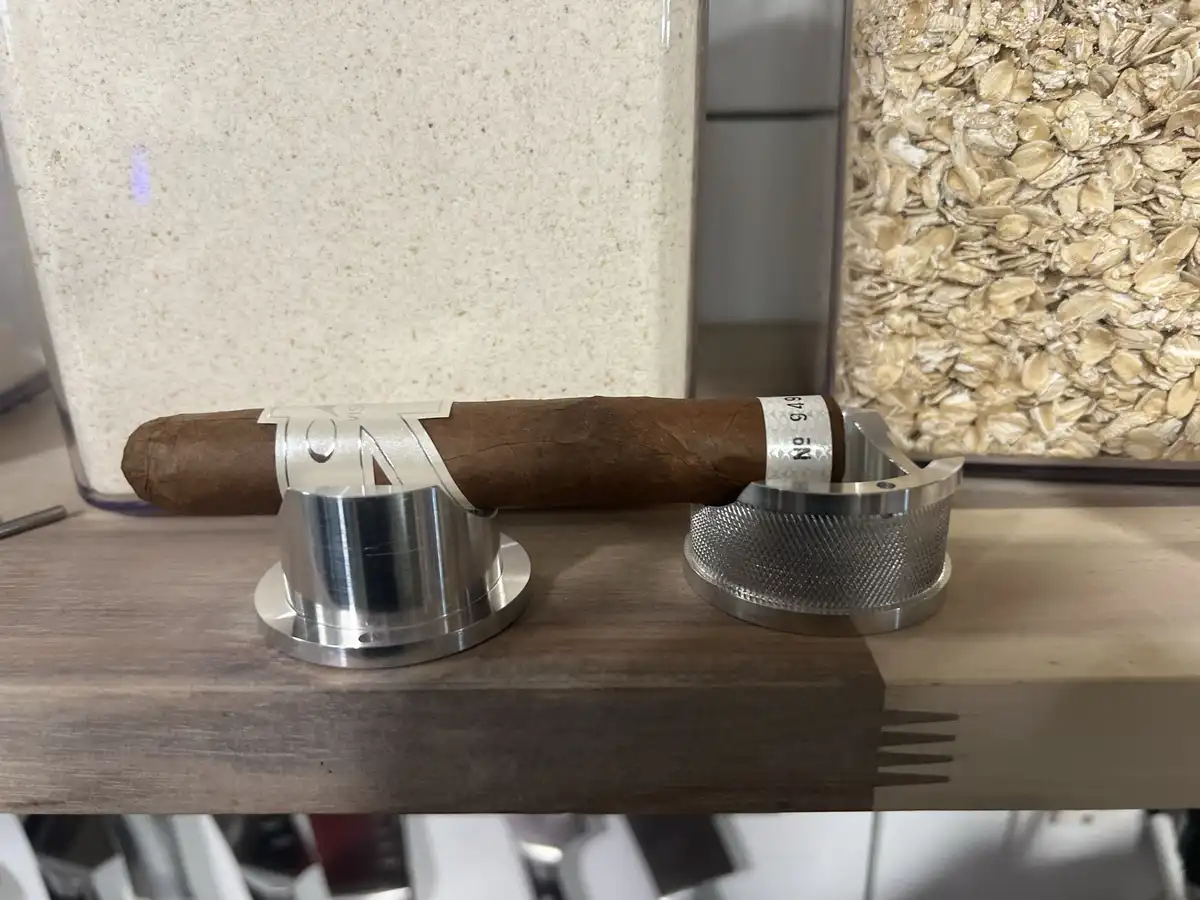 A brown cigar with a silver band labeled 'No 949' rests horizontally on a wooden surface, partially supported by two…