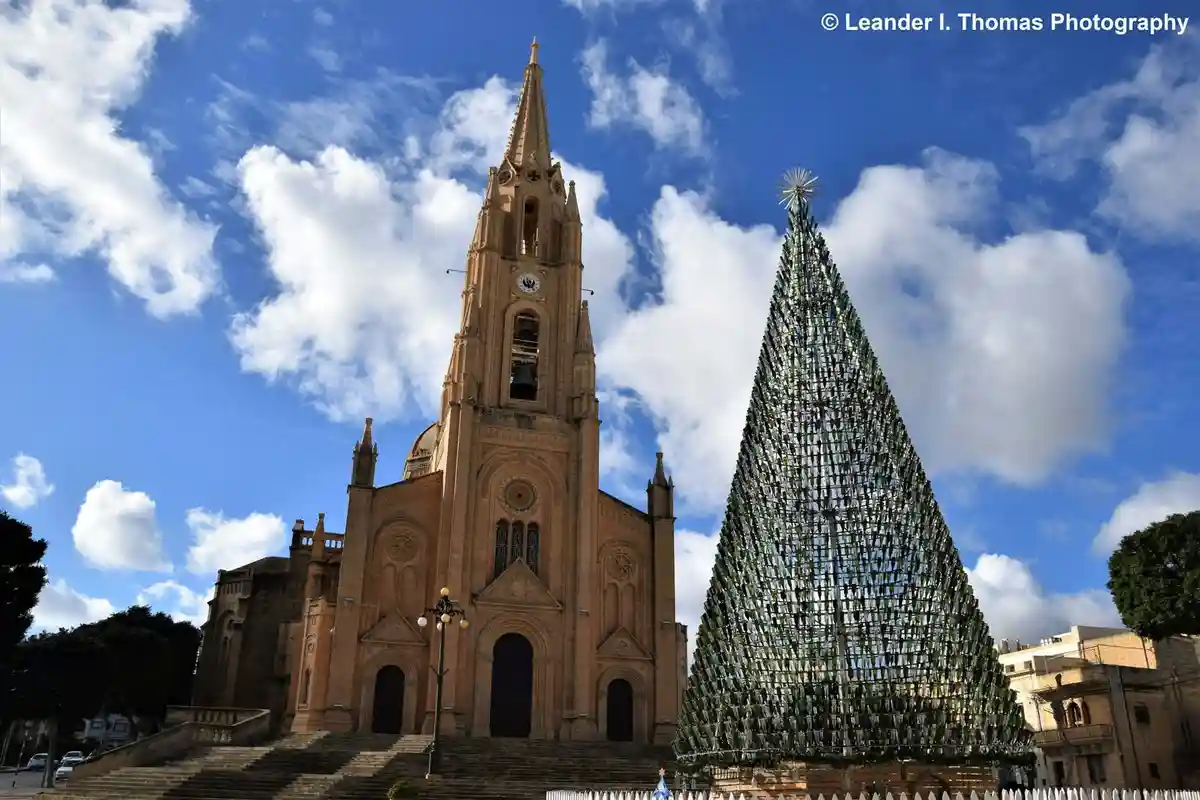 a large, ornate church with a tall spire stands beside a giant, cone-shaped Christmas tree constructed entirely from green…