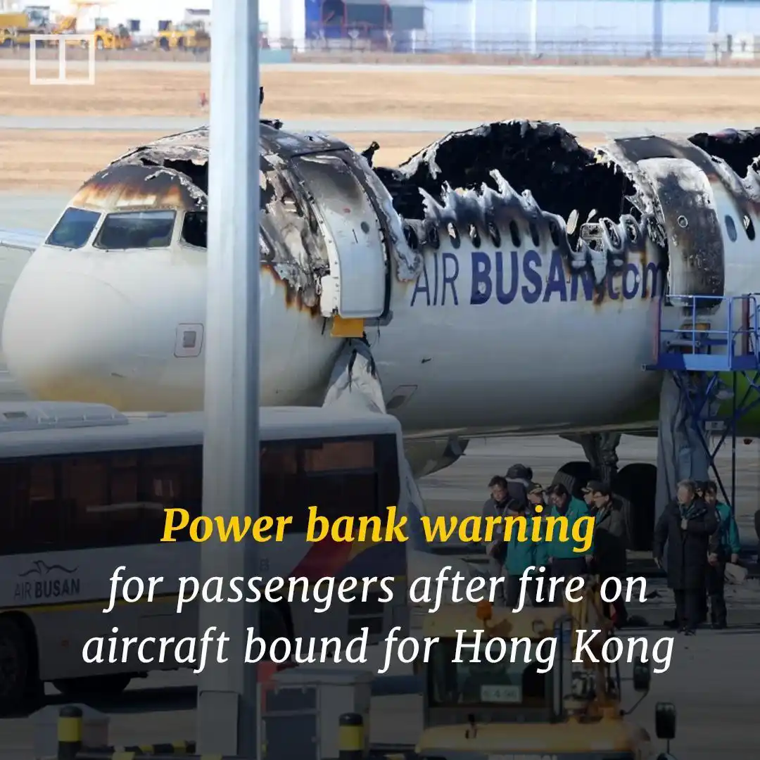 A severely damaged airplane with charred fuselage and missing sections, branded 'AIR BUSAN.com', sits on an airport tarmac…
