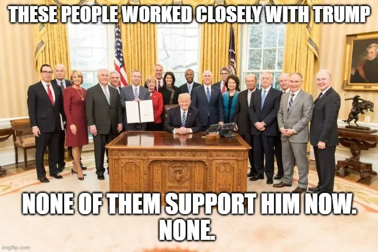 A group photo of numerous people, mostly in business attire, standing in the Oval Office behind a large wooden desk. A man…