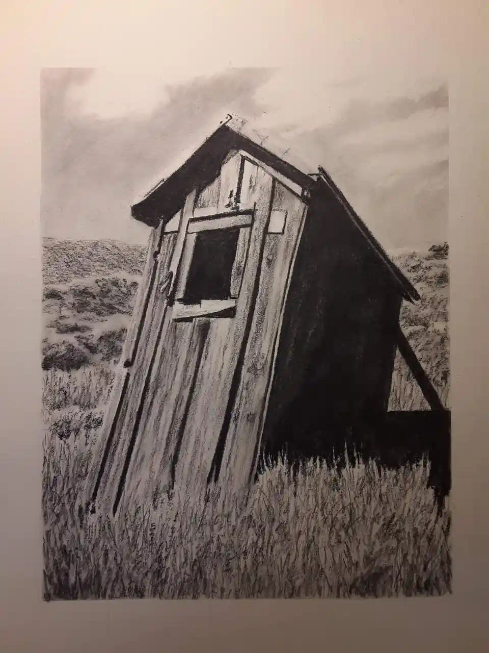 A black-and-white pencil drawing depicts a small, weathered wooden shed leaning precariously at a severe angle in a field of…