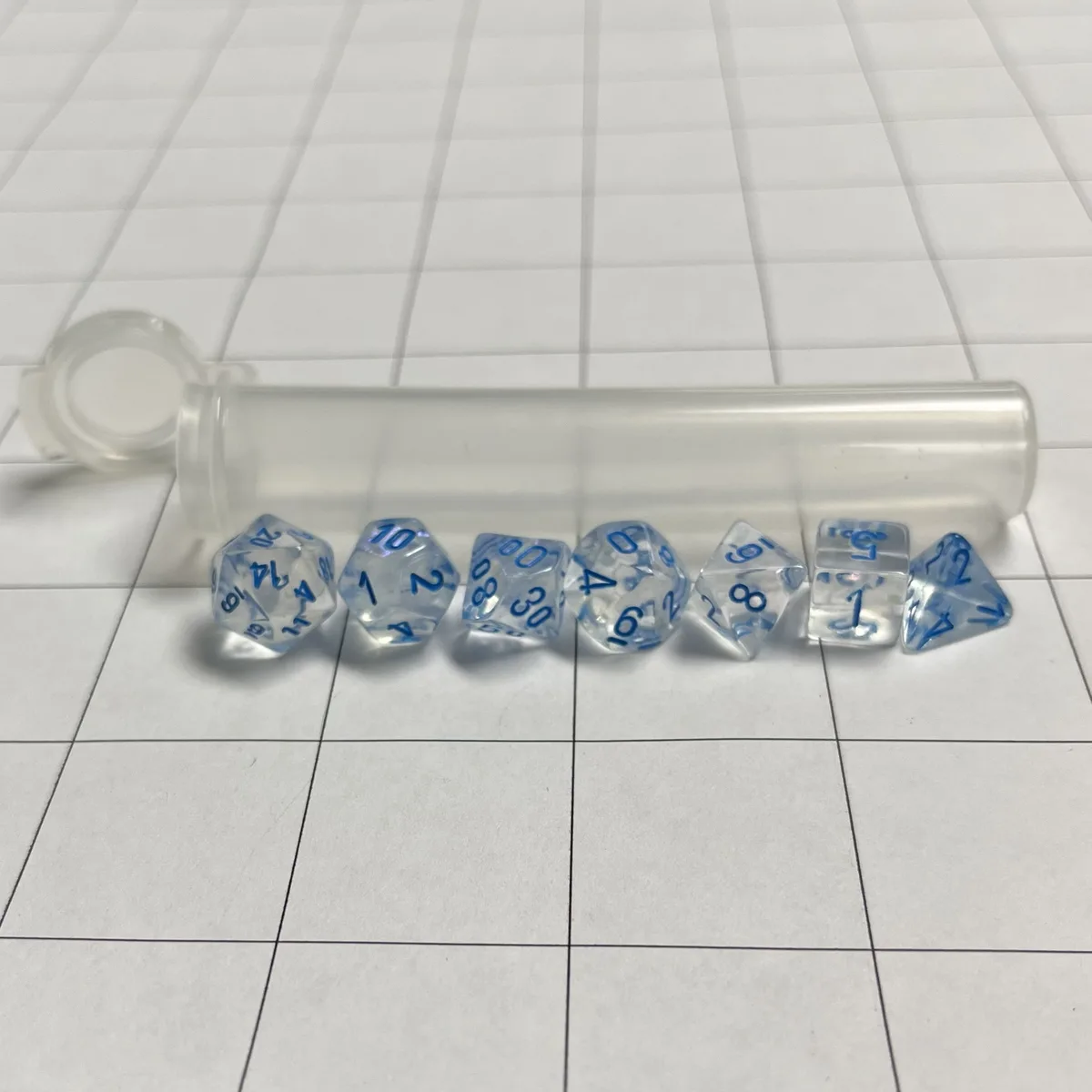 A row of transparent polyhedral dice with blue numbers, all showing the number one, are arranged in front of a clear plastic…