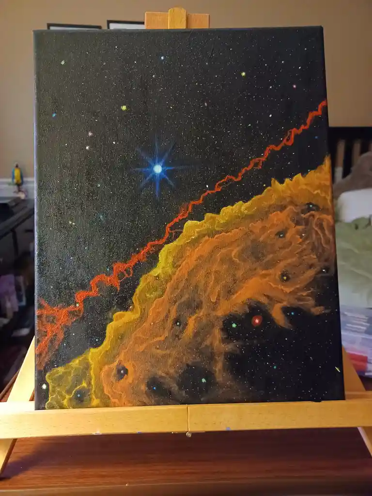 A hand-painted canvas on an easel depicts a cosmic scene with a black background, scattered stars, a bright blue starburst…