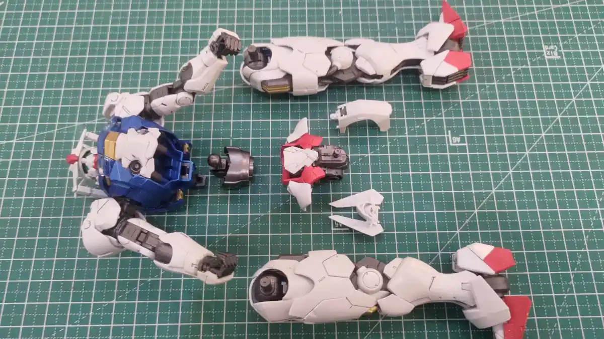 A disassembled white, blue, and red plastic robot model kit lies scattered across a green cutting mat with grid lines. The…