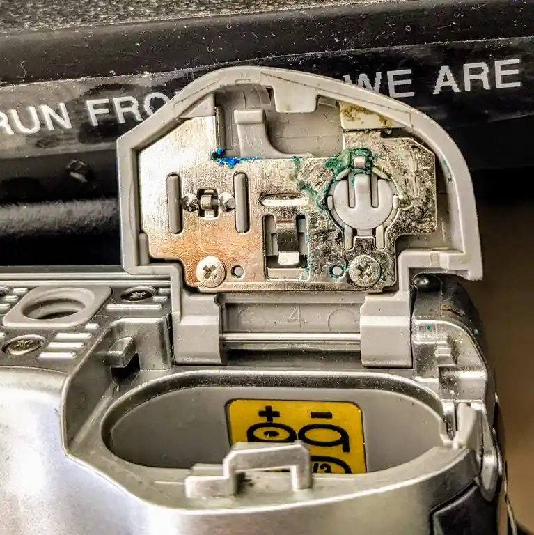 A close-up of a heavily corroded and dirty internal mechanism of a device, possibly a battery compartment or lock, with…