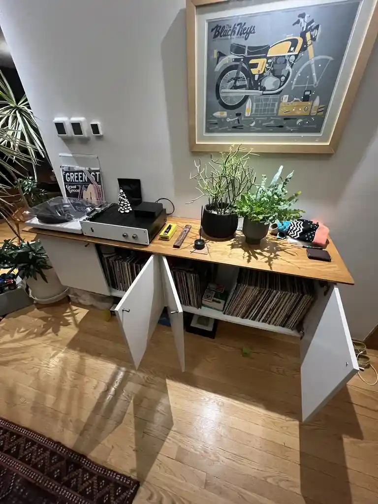 A wooden cabinet with white doors open, revealing shelves full of vinyl records inside. On top sits a record player, a small…