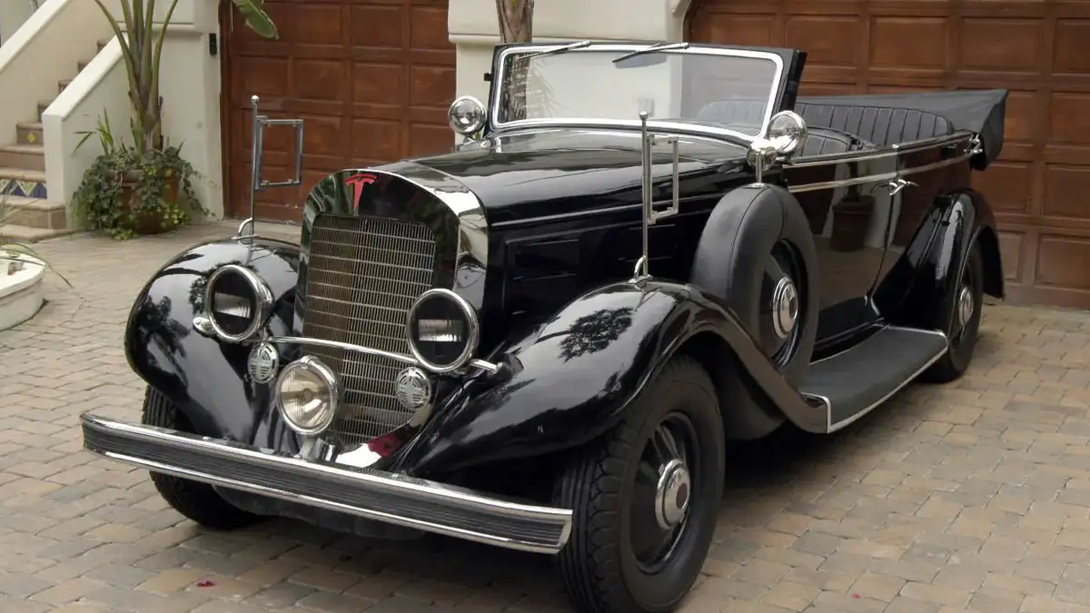 a black vintage-style convertible car with chrome accents and round headlights is parked on a brick driveway in front of a…